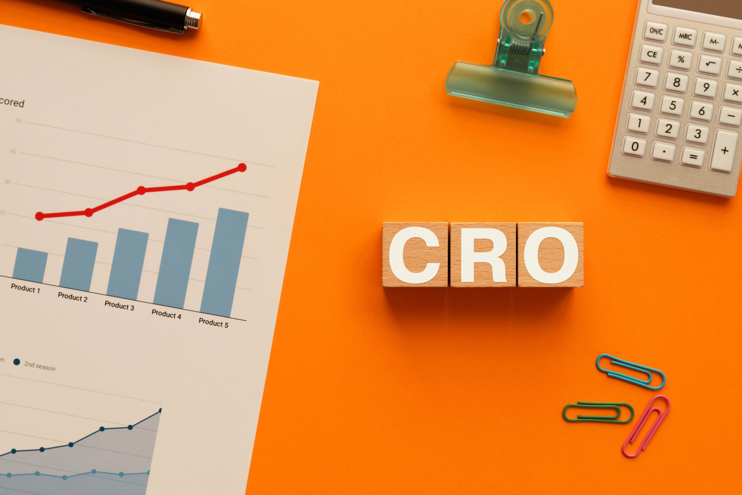 Conversion Rate Optimization concept with CRO letter blocks, business charts, calculator, and office supplies on orange background.